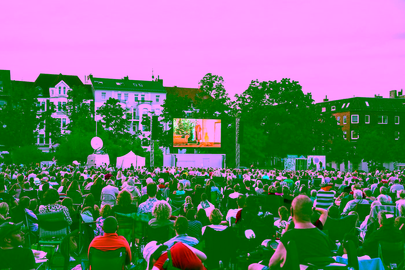 Publikum in Campingstühlen vor einer großen LED-Wand bei der Live-Übertragung der Kieler Sommeroper im Sonnenuntergang